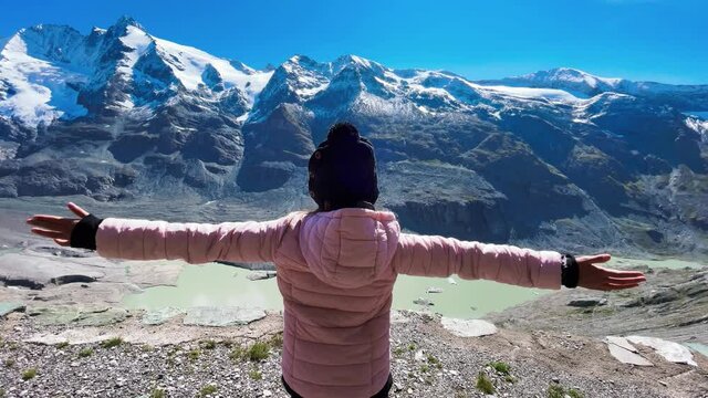 Back view of a young girl embracing fresh air with mountains covered by snow in summer season, Grossglockner National Park, Austria