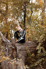 Fototapeta premium A girl with scary make-up in a skeleton costume sits on a withered old tree. Halloween