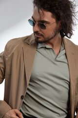 A young businessman in eyewear smiling broadly posing indoors. Male entrepreneur resting in the city street. The curly guy in casual wears spectacles with curly hair walking outside after work