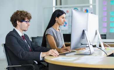 Businessman and businesswoman sitting and working together in front of desktop computer in modern office