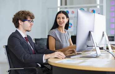Businessman and businesswoman sitting and working together in front of desktop computer in modern office