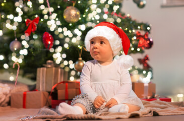 holidays and childhood concept - sweet baby girl with gifts at home over christmas tree lights