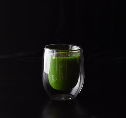 Green smoothie in a glass glass on a black background. Cooking healthy food.