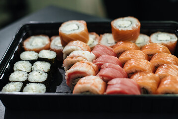 Japanese food concept. Catering, various kinds of sushi on plate. Placed on stone black background in plastic delivery box. Sushi roll (Philadelphia) with salmon, smoked eel, avocado, cream cheese.