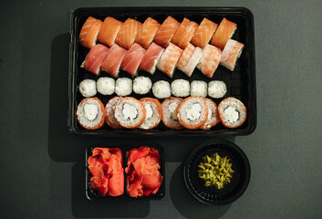 Japanese food concept. Catering, various kinds of sushi on plate. Placed on stone black background in plastic delivery box. Sushi roll (Philadelphia) with salmon, smoked eel, avocado, cream cheese.