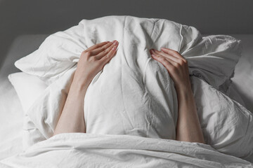 woman in bed hiding face under pillow