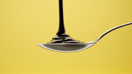 Melted chocolate is poured onto a steel spoon on a yellow isolated background