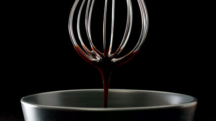 Liquid chocolate dripping from steel whisk on black background - 457083360