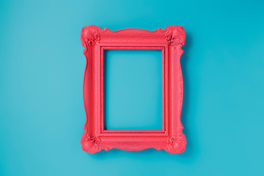 A pink empty frame isolated on the vibrant blue background. Decorative detail, retro inspired backdrop. Creative pop art antique frame concept. Juxtapose of and vintage and contemporary style.