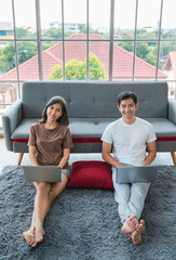 Young asian couple wearing comfortable t-shirt working with laptop together at home. Concept work...