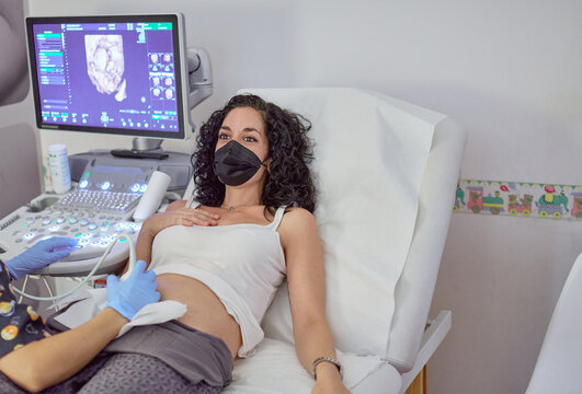 young pregnant woman with a face mask due to the coronavirus pandemic who is undergoing a gynecological ultrasound. concept gestation care and control of pregnancy