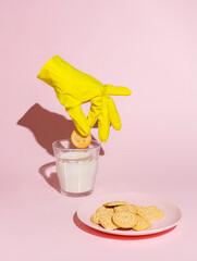Yellow sanitary glove holding a sweet biscuit and soaking in a glass of milk isolated on a pastel...