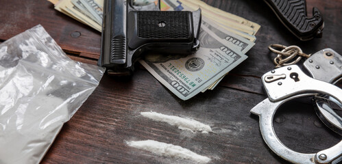 Drugs smuggling and trafficking, Handcuffs, pistol money and cocaine on wooden table background