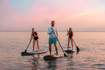 Group of caucasian people swimming on a sup boards at the ocean. Sport activity of friends at the vacation. Surfing - obrazy, fototapety, plakaty