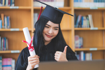 University graduate in graduation gown and mortarboard celebrates in a virtual graduation ceremony. Happy female student on her graduation day at home. Concept of online education