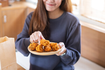 A young woman eating fried chicken from paper food bag in the kitchen at home for food delivery concept