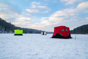 Ice fishing tent on a frozen lake at sunset. Fisherman camp on a peaceful winter evening.