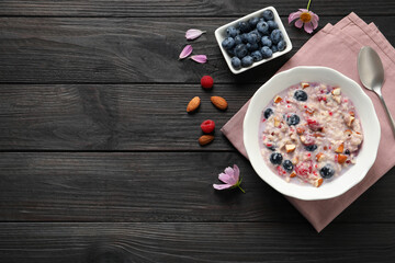 Tasty oatmeal porridge with toppings on black wooden table, flat lay. Space for text