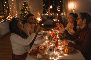 holidays and celebration concept - multiethnic group of happy friends with sparklers having...
