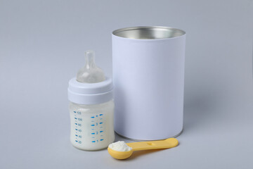 Blank can of powdered infant formula with scoop and feeding bottle on light grey background. Baby milk