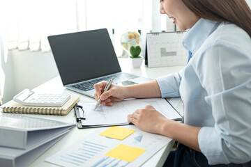 Woman office worker sitting to working and writing business project report on clipboard during checking information