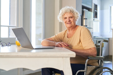 Happy elderly woman in wheelchair at laptop computer