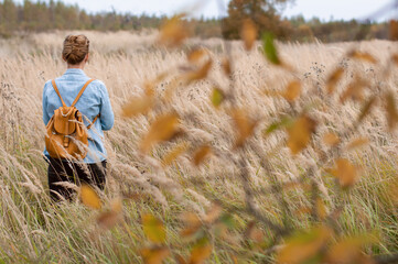 A young woman with a backpack on her back walks through the autumn field. Concept slow life.