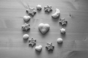 Different figures of ginger biscuits. Round pattern made of cookies on wooden background. Christmas cookies, stars, hearts, moon and big heart is in the center. Black and white high-quality photo