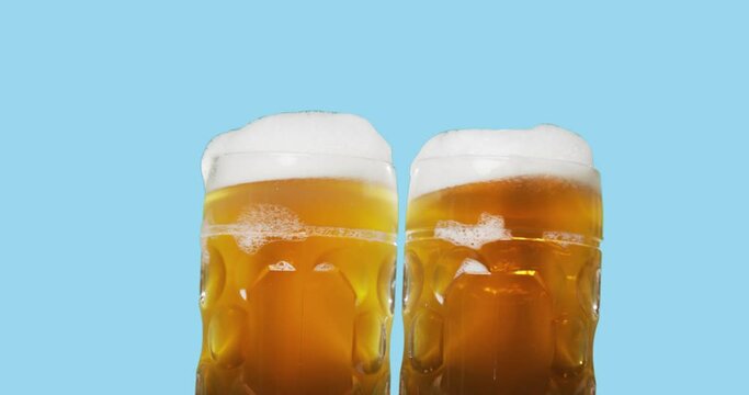Celebration beer cheers concept - close up two swaying mugs or glasses of beer with foam isolated over abstract color background. Oktoberfest traditional party or victory competition or successful tas