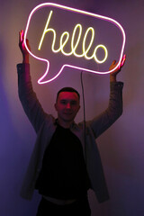 Handsome young man holding pink and yellow neon sign hello. Trendy style. Neon sign. Custom neon. Home decor.