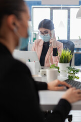 Executive manager talking at landline explaining marketing strategy to collegue working at company report in startup office. Businesswoman with medical face mask against covid19 during global pandemic