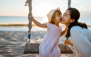 daughter kissing her mother while swinging at the beach