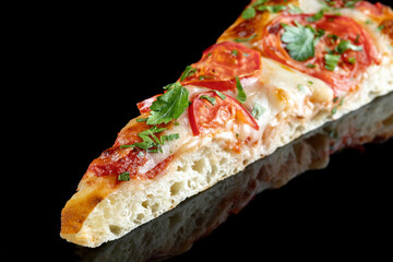 Slice of pizza with tomatoes and parsley, on a black mirrored background. Beautiful light, product reflection.