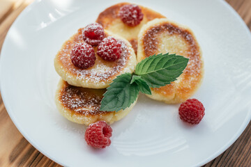 Delicious cheesecakes or pancakes with powdered sugar on white plate on wooden table with raspberries and mint leaf - Powered by Adobe