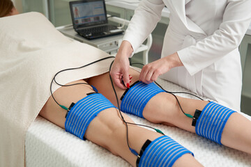 The procedure of myostimulation on legs of a woman in a beauty salon. Caring for the body with...