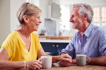 Retired Couple Sitting Around Table At Home Having Morning Coffee Together