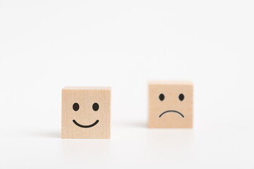 Close up of a smiley face and blurred sad face icon on the wood cube,isolated on white background , Service rating, satisfaction concept.