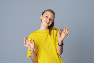 Beautiful glad teen girl shows ok gesture both hands, isolated on light gray background
