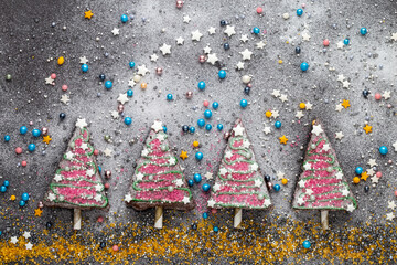 Vier süße Kuchenstücke in der Reihe dekoriert als Christbäume mit Zuckerperlen, Sternen und...