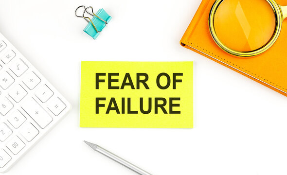 Sticker with the text FEAR OF FAILURE on a white background, near calculator and notebook