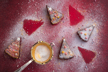 Vier von sieben Stück weihnachtlichem Gebäck dekoriert mit Zuckerperlen und Sternen, goldenem Sieb mit Puderzucker auf rotem Grund