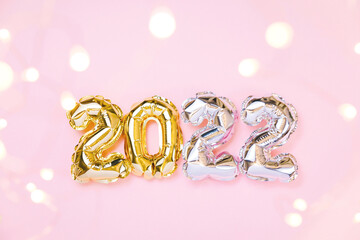 Happy New year 2022 celebration. Gold and silver foil balloons numeral 2022 and fairy lights on pastel pink background. Flat lay, christmas creative concept