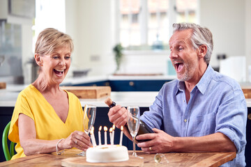 Fototapeta na wymiar Retired Couple Celebrating Birthday With Glass Of Champagne And Cake At Home Together