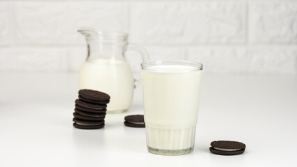 full glass cup of milk, next to a stack of round chocolate chip cookies on a white table