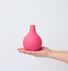 hand holds a pink rubber enema on a white background