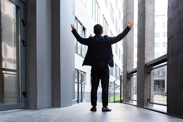 Successful businessman raises his hands up a sign of victory and success near the modern office back view