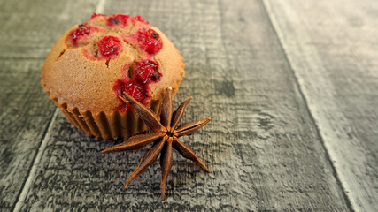 on the left, gluten-free chocolate muffins with red currants and a brown star of anise on the background of a wooden table. side view