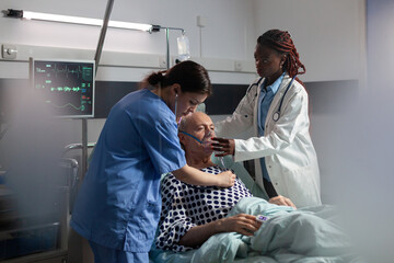 Obraz na płótnie Canvas African doctor helping senior patient breath using repiratory ventilation tube, in hospital room intensive care. Old man hospitalized checked by medical staff and getting treatment.