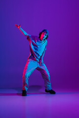 Stylish sportive boy dancing hip-hop in stylish clothes on colorful background at dance hall in...