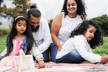 Happy indian family having fun painting with children outdoor at city park - Focus on boy face